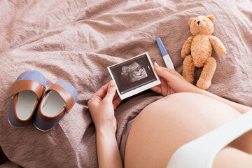 Pregnant Woman sitting on bed and Looking At Ultrasound Scan photo of her Baby. A pregnant female...