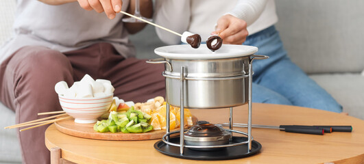 Young couple dipping marshmallows into chocolate fondue at home