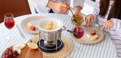 Young couple eating snacks with cheese fondue and glasses of wine at home
