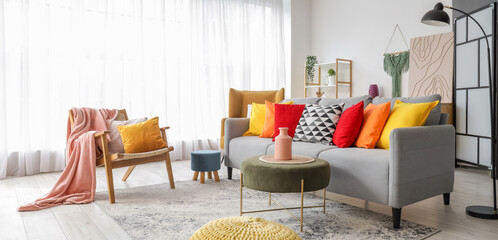 Interior of stylish living room with colorful cushions on sofa, armchair and poufs