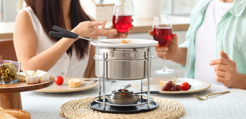 Cheese fondue on table of young couple drinking wine in kitchen