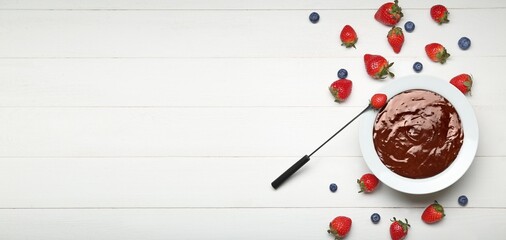Bowl with tasty chocolate fondue and berries on white wooden background with space for text