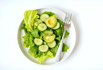 Flatlay of fresh green salad with lettuce, cucumber, and avocado slices, served on white ceramic plate with stainless fork. Clean background, bright natural light, minimal and healthy.