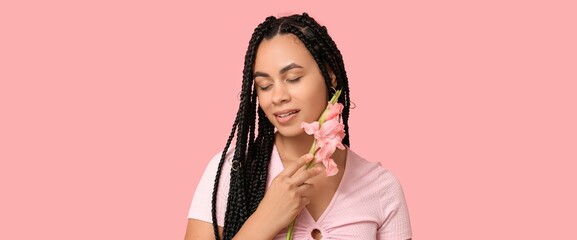 Beautiful young African-American woman with gladioluses on pink background