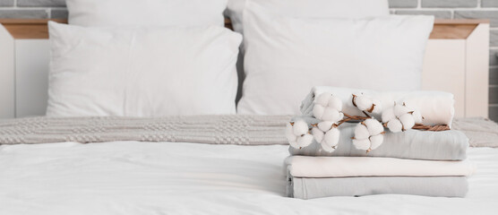 Stack of clean bed sheets with cotton flowers sprig in bedroom