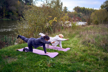 middle-aged woman teaches her old mother somatic exercises and yoga to maintain health by the river...