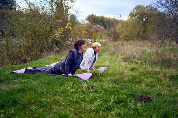 middle-aged woman teaches her old mother somatic exercises and yoga to maintain health by the river in autumn