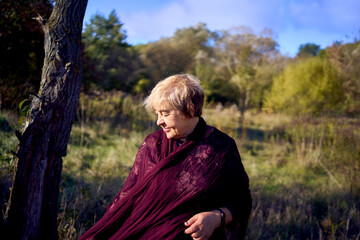 portrait of an elderly woman with gray hair in a dress and shawl in the autumn forest