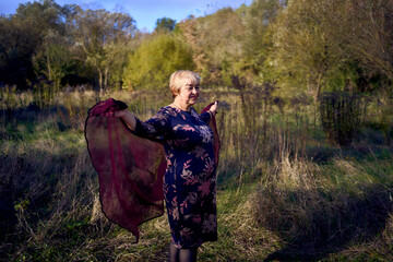 portrait of an elderly woman with gray hair in a dress and shawl in the autumn forest