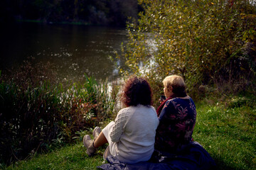 middle-aged daughter and old mother eating pastries and drinking tea from thermos cups on a picnic in the autumn forest