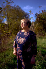     a   portrait of an elderly woman with gray hair in a dress  in the autumn forest