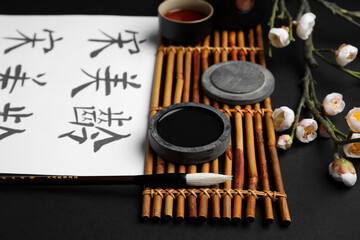 Paper sheet with Asian hieroglyphs, brush, ink and blooming branch on dark background, closeup....