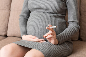 Close-up of pregnant woman is holding a cigarette sitting on sofa at home