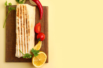 Board with tasty shawarma and ingredients on yellow background