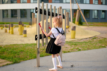 girl playing outdoor xylophone in school playground. child enjoying music with mallets in hands....