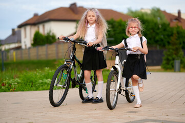 girls in school uniforms riding bicycles on suburban street. young cyclists enjoying outdoor...