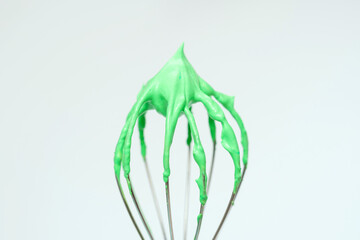 Whisk with green whipped cream from proteins close-up on gray background.