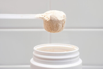 Protein powder in scoop from plastic jar side view on gray background close-up.