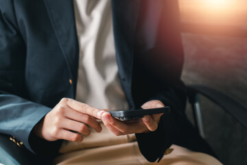 Obraz premium Close-up of a business professional using a smartphone in an office environment with warm sunlight.