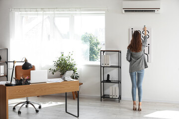 Young businesswoman turning on air conditioner in office, back view
