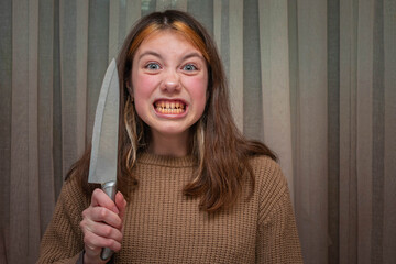 Portrait of a girl with a knife in her hands. Evil teenage girl shows teeth and knife.