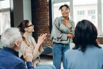 Smiling African American woman receiving applause from support group members clapping