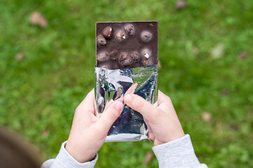 Child's hands opening a foil-wrapped chocolate bar with nuts outdoors.