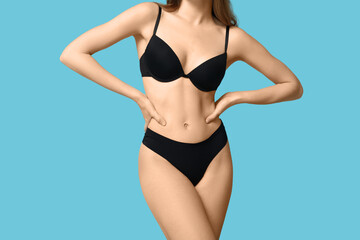 Fototapeta premium Attractive young woman in black underwear on blue background