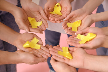 People with yellow awareness ribbons on pink background, closeup. World Cancer Day