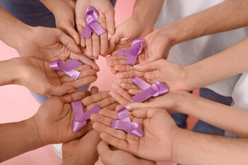 People with lavender awareness ribbons on pink background, closeup. World Cancer Day