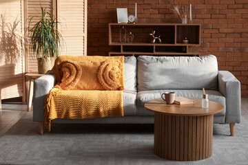 Interior of cozy living room with grey sofa, table and shelf unit at sunset