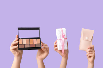 Female hands with eyeshadows palette, gift box and case for brushes on lilac background