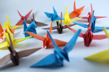 A colorful array of red, orange, yellow, blue, and brown origami cranes scattered across a clean...