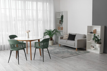Interior of modern living room with table, chairs, sofa, houseplants and shelving unit