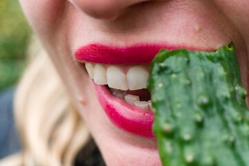 Woman with red lipstick biting a green vegetable.