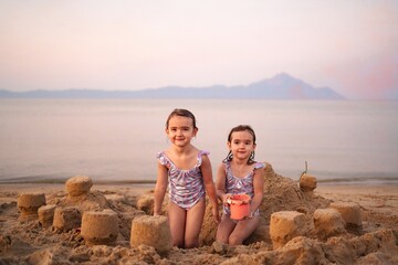 Joyful sisters building sandcastles on a serene beach at sunset