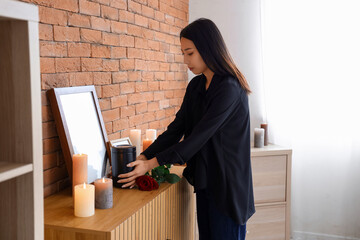 Grieving young Asian woman with mortuary urn at funeral