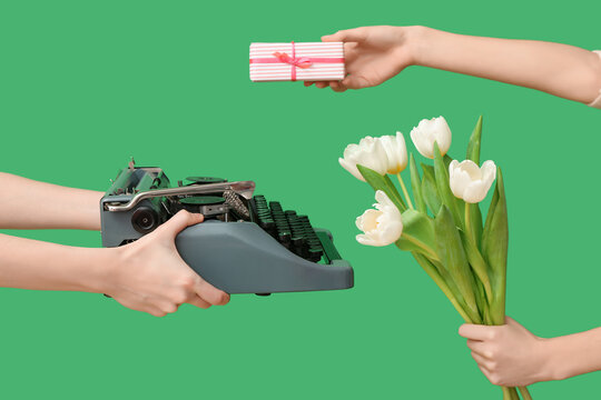 Female hands with retro typewriter, tulip flowers and gift for International Women's Day on green background, closeup