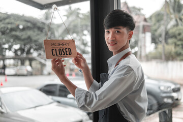 Cheerful young man hangs closed sign, urban shopfront, candid moment, city life, positive vibe
