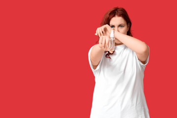 Beautiful young woman with bottle of sanitizer on red background