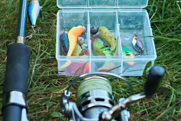 Box with fishing lures on the background of a spinning reel. Fishing gear. Selective focus.