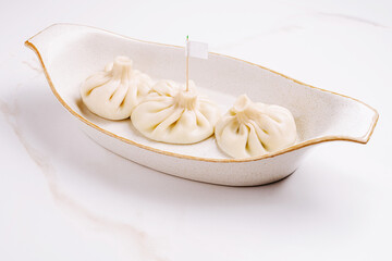 Three traditional Georgian khinkali dumplings arranged in a cream-colored ceramic dish,...