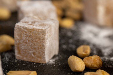 Turkish delight on the table, sugar cubes with starch and toasted peanuts on a black surface, close up