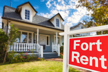 Red for rent sign in front of charming house with white trim and lush lawn under clear blue sky
