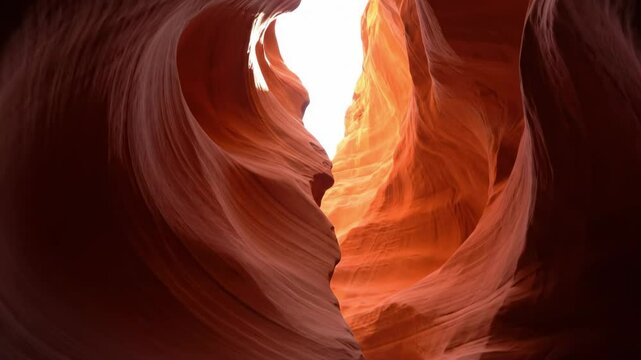 A slot canyons curving layered sandstone walls create a narrow passage with bright light at the top