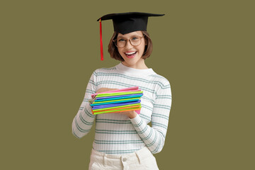 Beautiful student in graduation hat with copybooks on green background