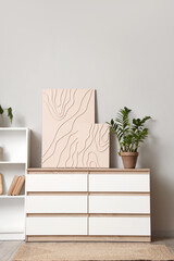 Stylish paintings with plant on commode in light room