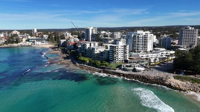 Aerial cityscape of Cronulla with sandy beach, turquoise water and skyline in sunlight, establishing pullback, Sydney NSW Australia