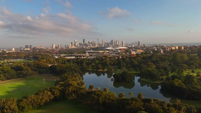 Aerial panoramic establishing of Centennial Park with skyline in background and lush trees under blue sky, Sydney NSW Australia