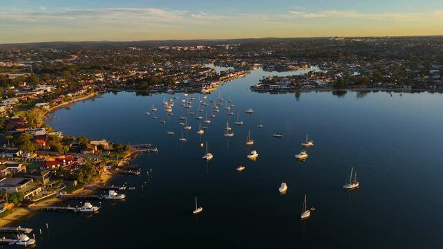 Aerial of luxury homes on canals in Sylvania Waters with sailboats and yachts anchored in tranquil setting, Sydney NSW Australia